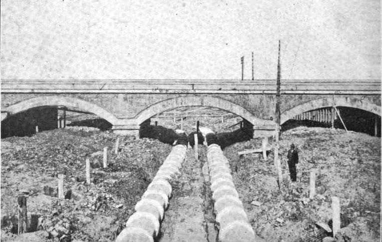 Due grandi tubi passano sotto le arcate del ponte ferroviario