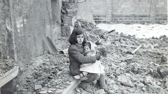 Una bambina con un bimbo in braccio seduta sulle macerie nel 1944