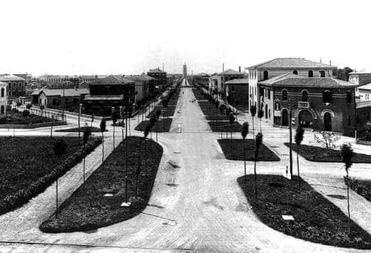 Viale alberato del quartiere urbano di Marghera con le prime case e un serbatoio sullo sfondo