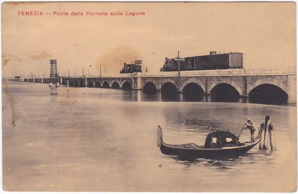 Cartolina d'epoca del ponte ferroviario sulla laguna di Venezia con un treno a vapore e una gondola in primo piano